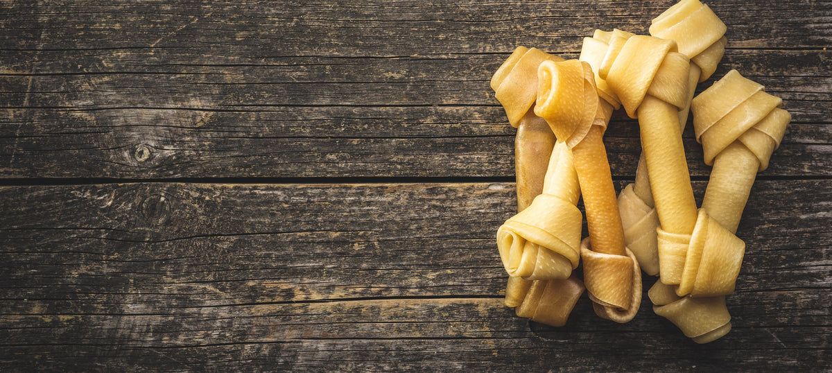 Several knotted rawhide bones arranged on a dark rustic wooden surface