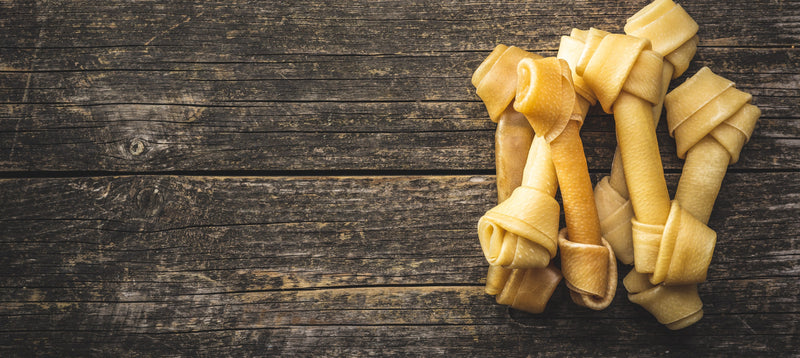Several knotted rawhide bones arranged on a dark rustic wooden surface